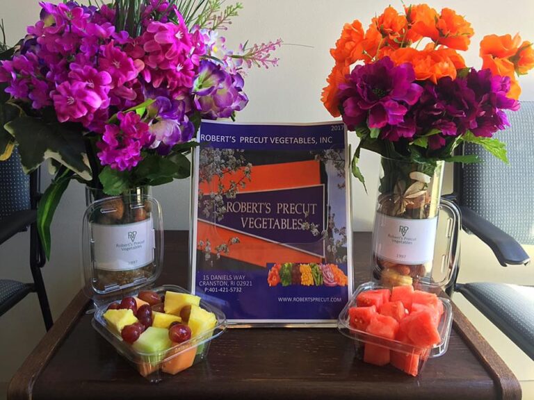 Bowl of fruits with colorful flowers around kept on a wooden table